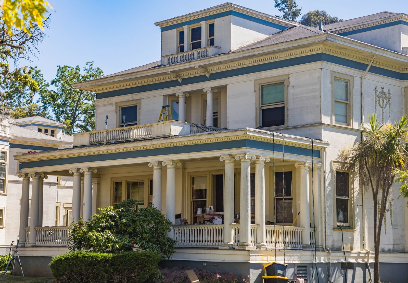 Grand colonial mansion with classic columns and lush greenery in a sunny outdoor setting.