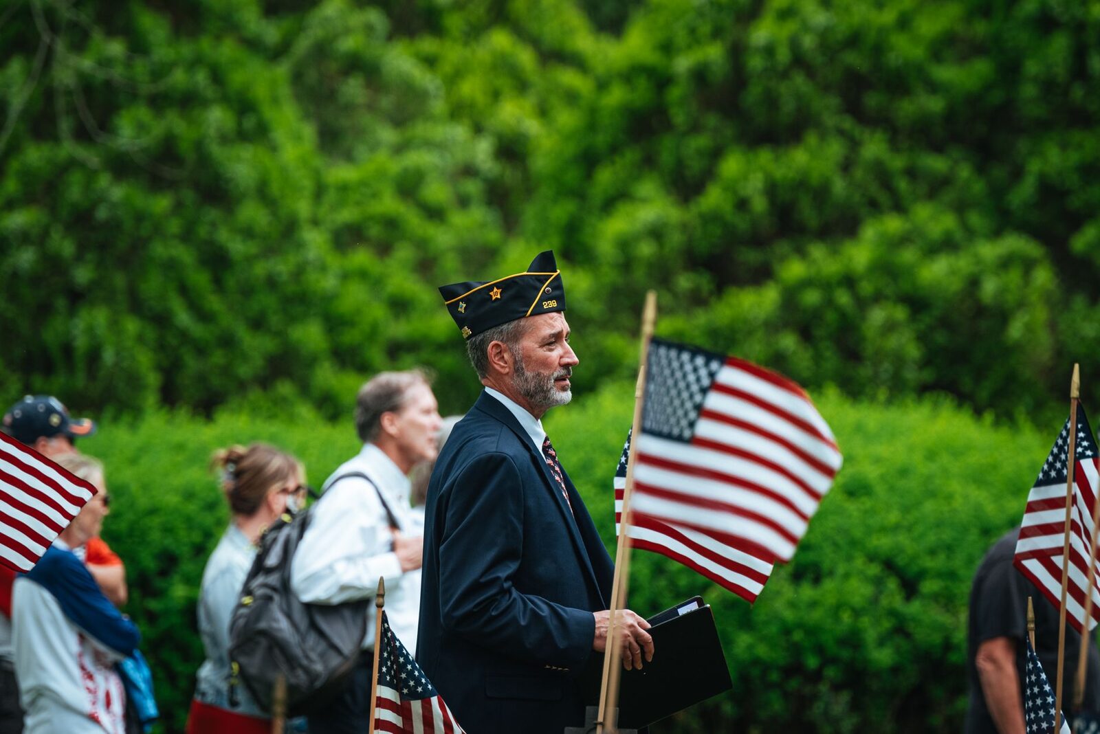 A veteran leads a patriotic parade outdoors, surrounded by American flags in a summer setting.